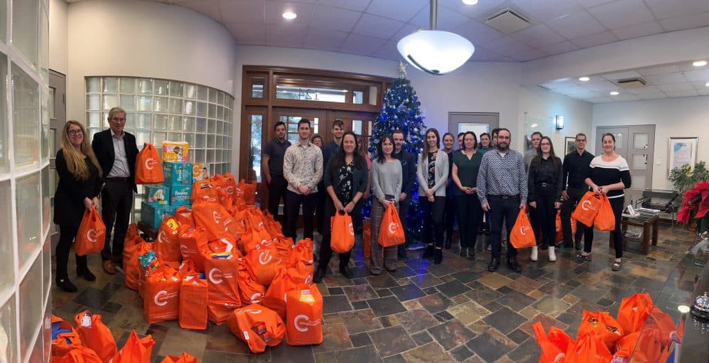 Orange gift bag carriers in front of a Christmas tree as a team, Christmas distribution, solidarity, gift wrapping, festive atmosphere, Christmas, community action, team of volunteers, charity event, festive solidarity.