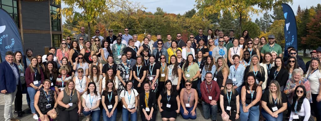 Grand groupe de participants lors d'une conférence ou événement professionnel, avec décor automnal en arrière-plan, représentant la communauté Amyot Gelinas.