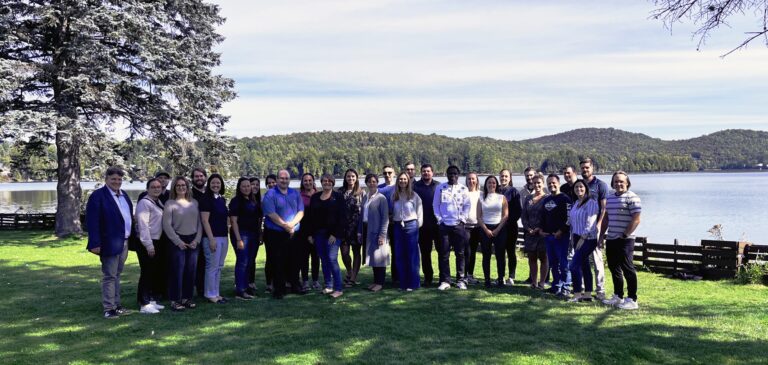 Group of people meeting outdoors by a lake, natural landscape and mountains in the background, friendly atmosphere, ideal for professional networking.