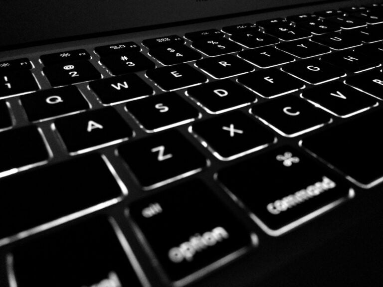 Backlit computer keyboard in black and white, featuring illuminated keys, ideal for work or programming.
