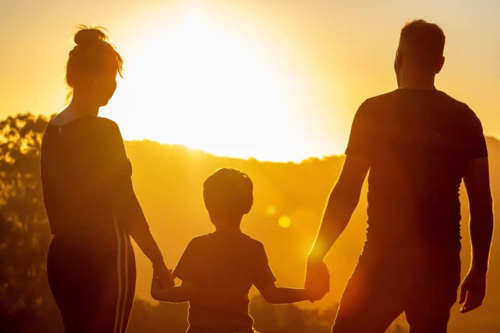 Silhouette d'une famille tenant la main lors d'un coucher de soleil, symbolisant la famille heureuse et l'amour.