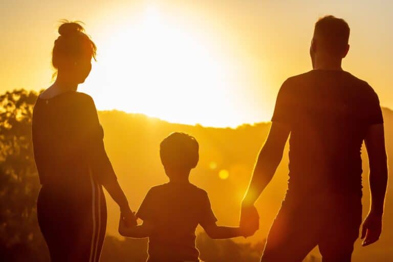 Silhouette d'une famille tenant la main lors d'un coucher de soleil, symbolisant la famille heureuse et l'amour.