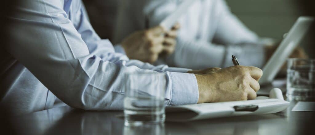 Note-taking in a business meeting, person wearing a blue shirt, professional environment, concentration and teamwork.