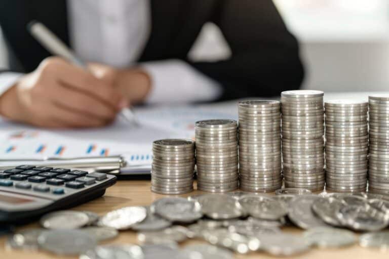 Piles de pièces de monnaie argentées, calculatrice et documents financiers sur un bureau, illustrant la gestion financière et l'investissement.