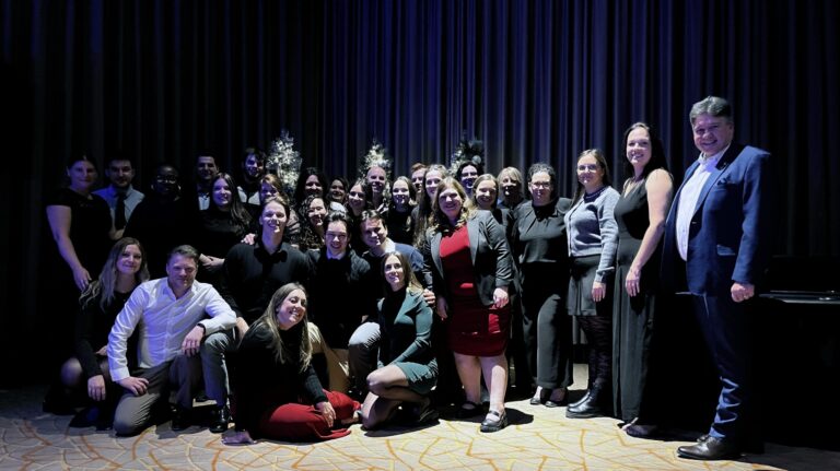 Une groupe de personnes posant sur scène lors d'une soirée des Fêtes 2025, avec Amyot Gelinas, ambiance festive et élégante, sous un rideau bleu foncé.